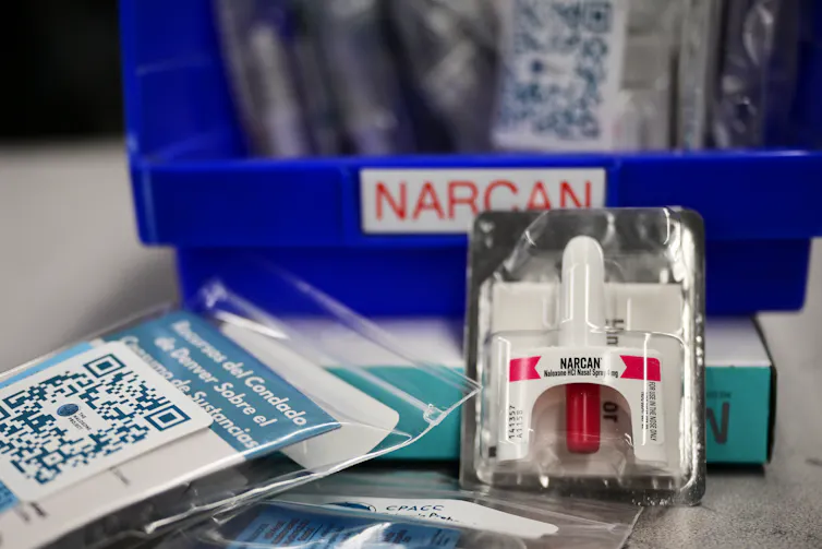 A white bottle of naloxone in a package sits in front of a blue bin.