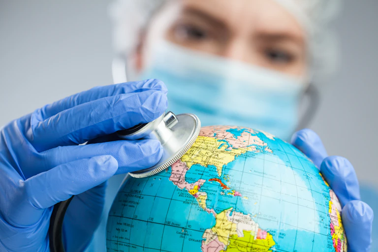 Une soignante avec un masque chirurgical pose un stéthoscope sur une mappemonde.