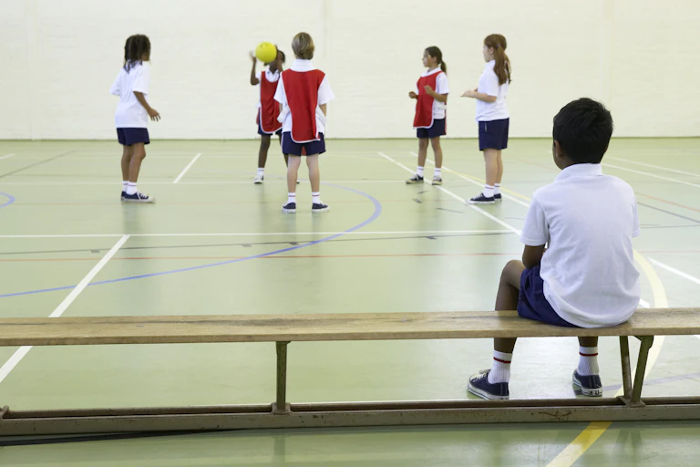 Child sitting on bench watching other children play with a ball