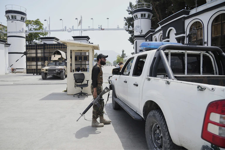 A man talks to another man inside a car in front of a security checkpoint.