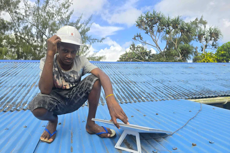 Man wearing hardhat and touching a small Starlink kit, on top of a corrugated iron roof.