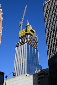 A shiny skyscraper is partly clad with a yellow construction crane on top