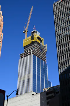 A shiny skyscraper is partly clad with a yellow construction crane on top