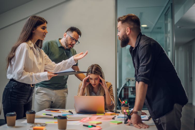 people in an office stand around a table arguing