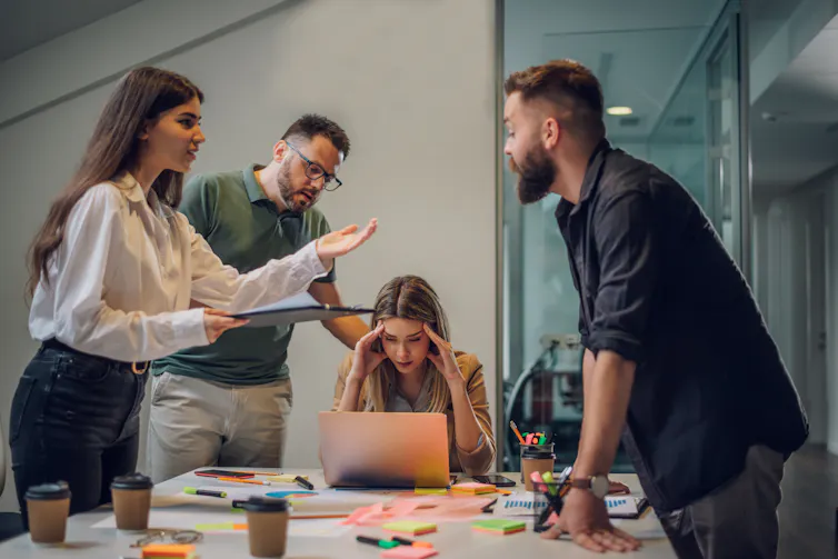 people in an office stand around a table arguing