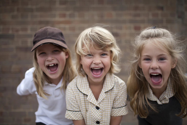 Three children yell, standing in front of a brick wall
