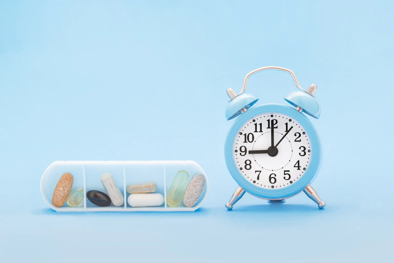 Un pastillero junto a un reloj despertador