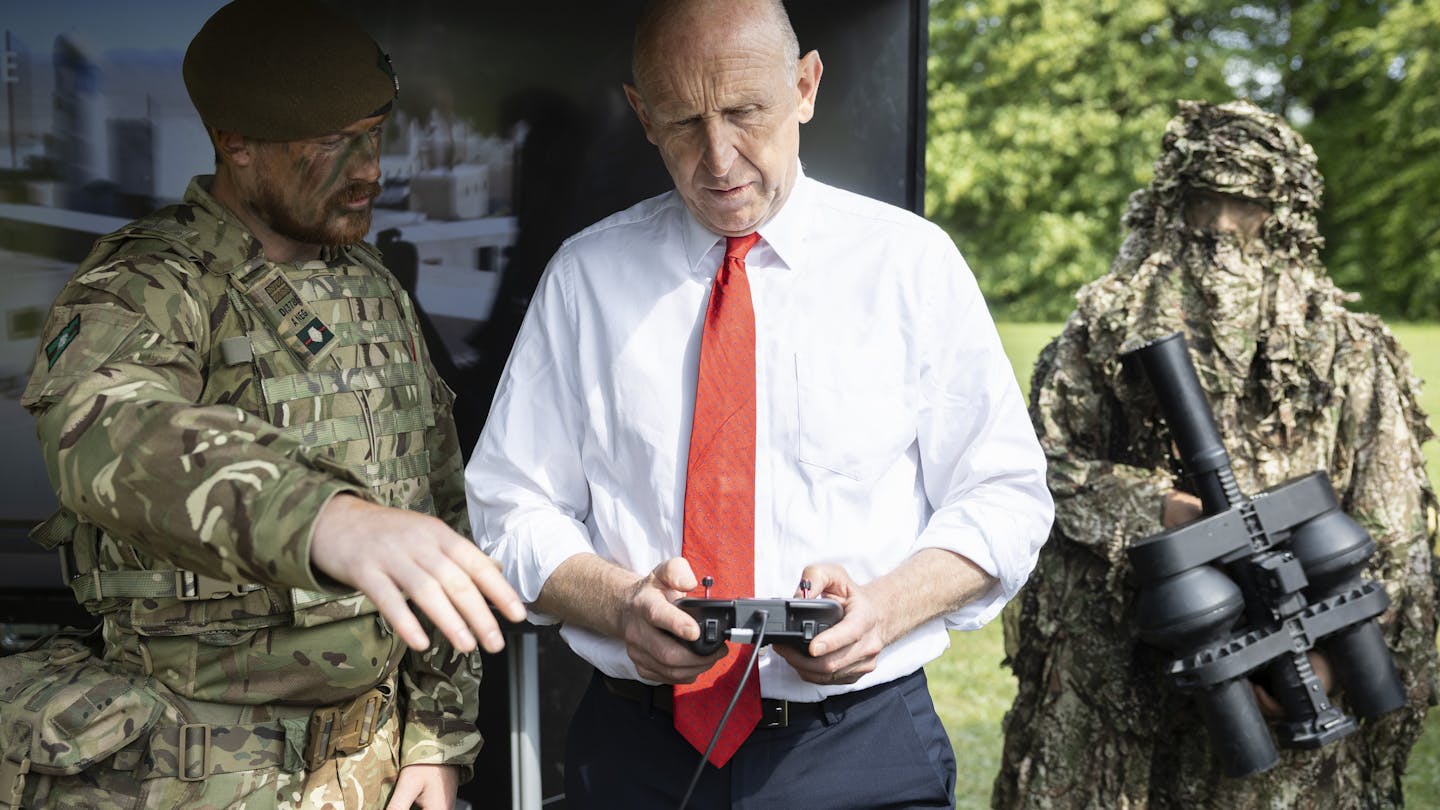 A soldier explains to john healey, who is holding a controller