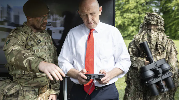 A soldier explains to john healey, who is holding a controller