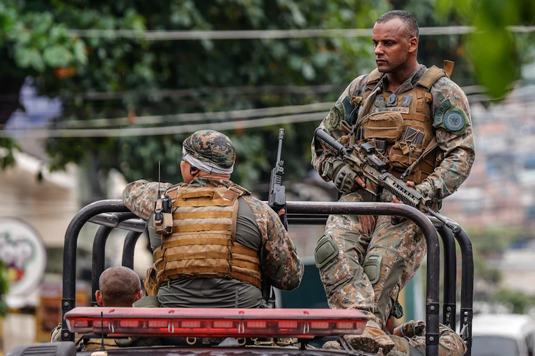 Brazilian military personnel sat on the back of a vehicle.