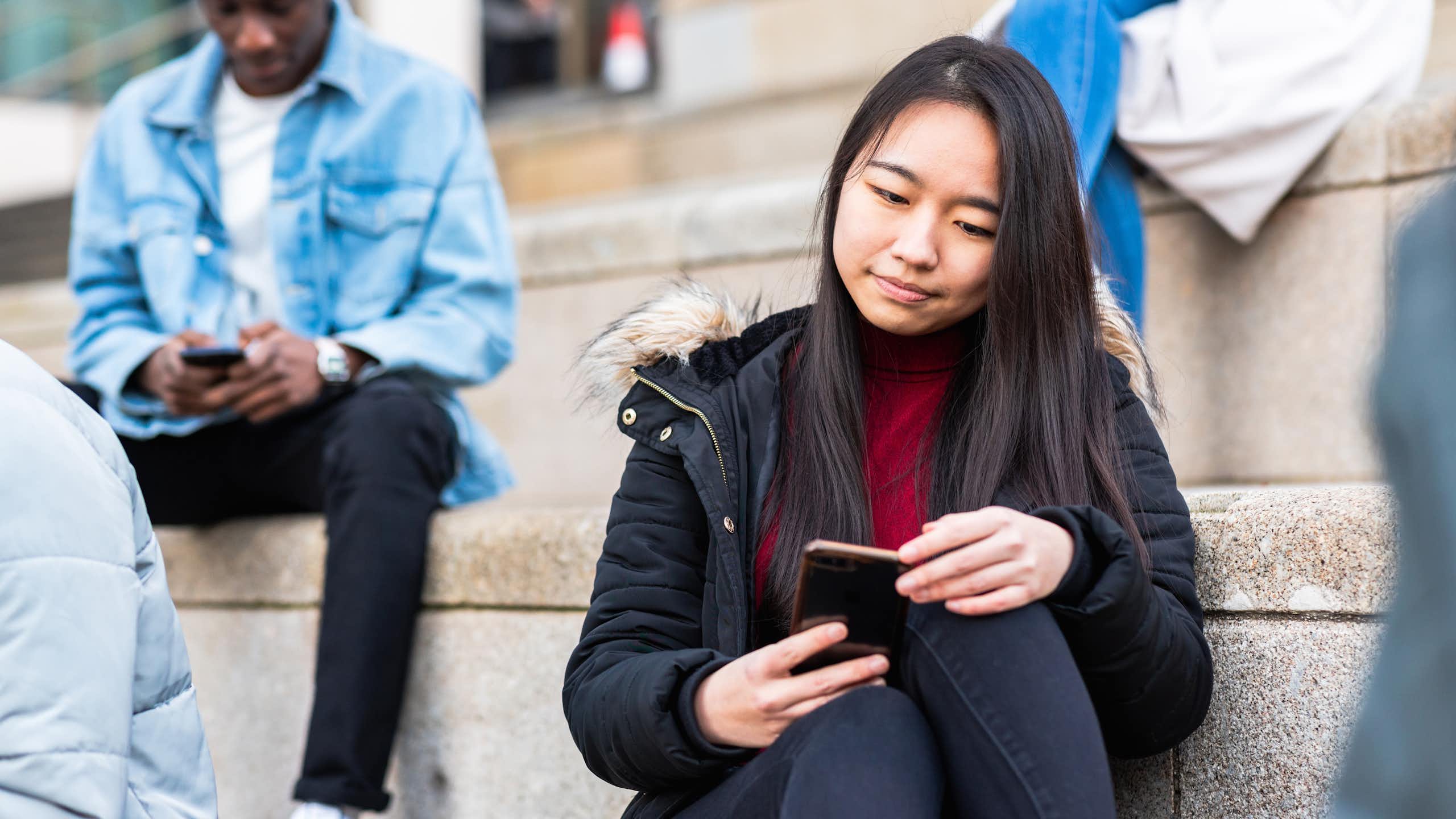Una chica sentada en unas escaleras consulta su móvil