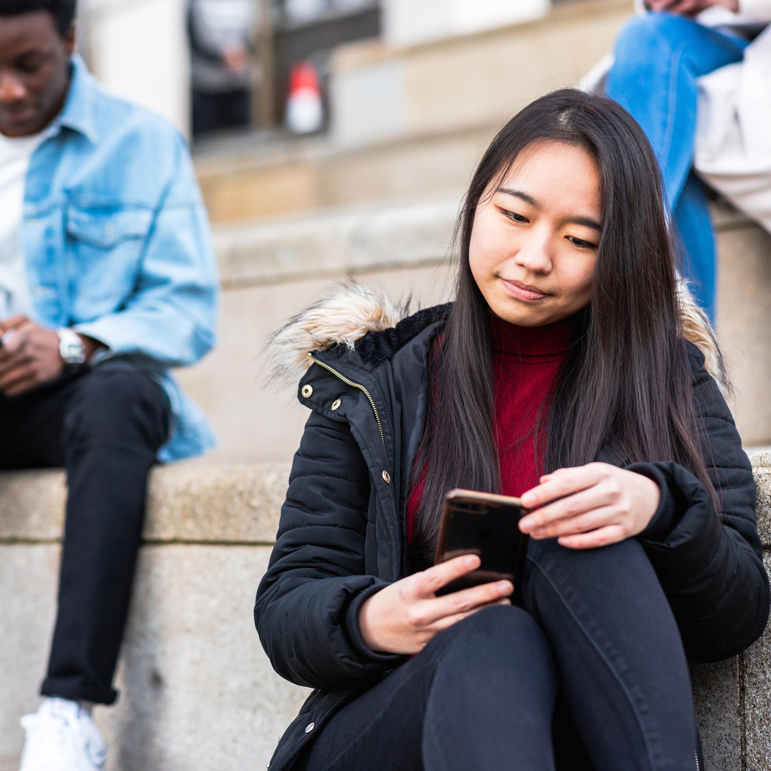 Una chica sentada en unas escaleras consulta su móvil