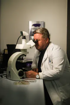 Michael Cunliffe wearing white lab coat looking down big micrscope