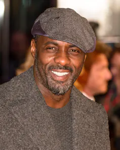A handsome black man smiling at the camera wearing a flat cap.