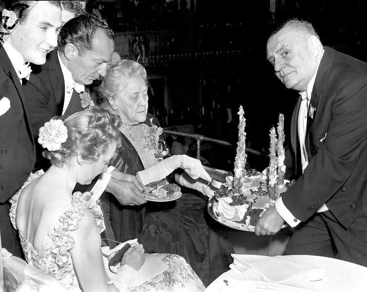 The Waldorf Astoria: what the historical past of this mythical lodge says about these days’s disaster of the American status quo 2 Black and white photo from 1940 of a grey haired lady cutting a birthday cake.