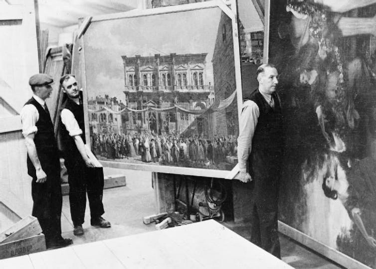Two men carrying a large painting.
