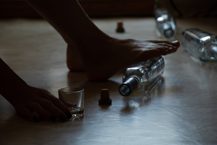 Close-up of foot stepping on empty alcohol bottle and hand grasping a shot glass, other empty bottles surrounding