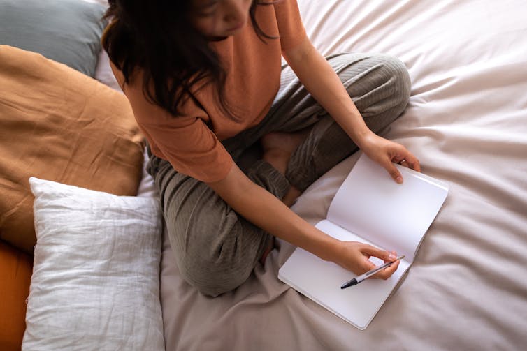 woman sitting on a bed and writing in a journal