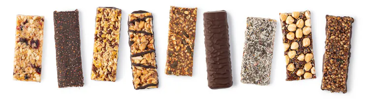 Nine different unwrapped granola bars, some of which have chocolate coating or drizzle.