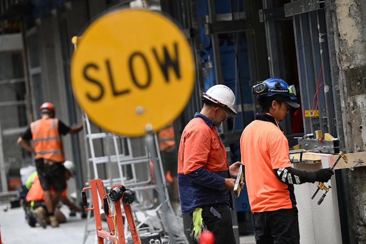 Several workers wearing hi-viz with a traffic saying 'slow'