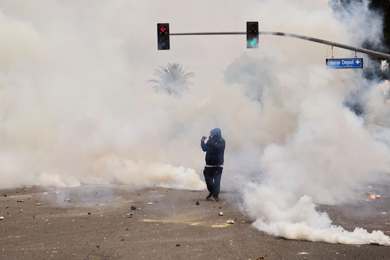 Smoke billows around a man wearing a parka and face mask in the middle of a city street.