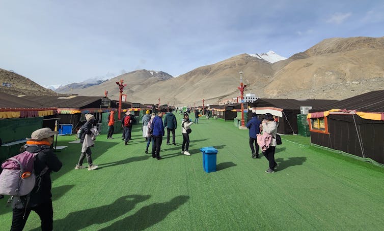 Tourists walking on a green astroturf walkway at Everest's northern base camp.