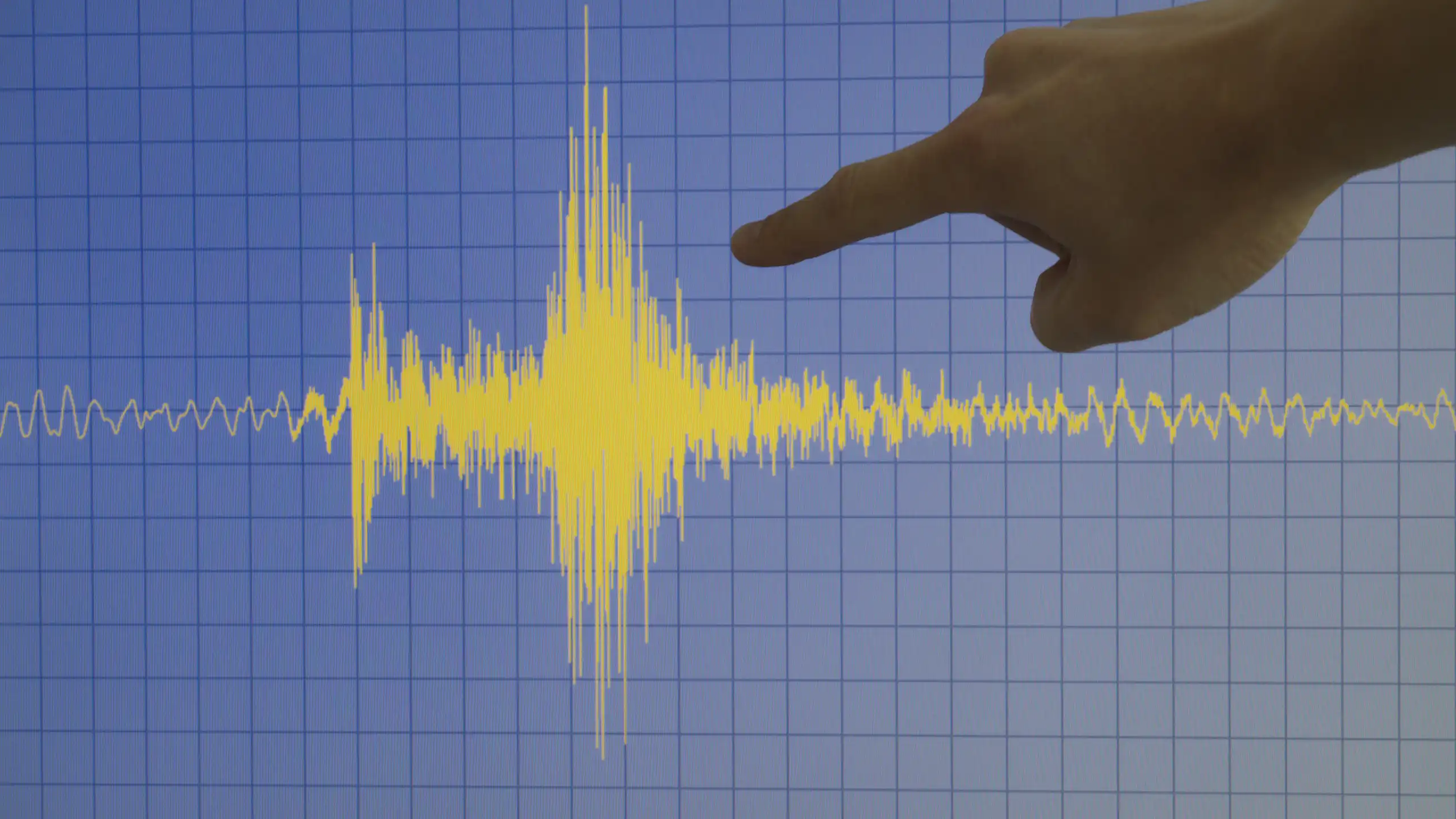 Una mano señala una oscilación en un sismógrafo