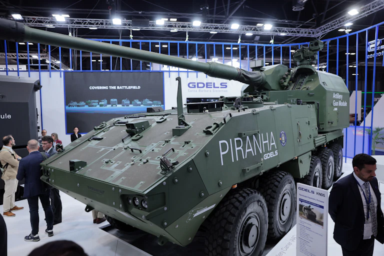 A green artillery carrier is seen on the floor of a trade show.