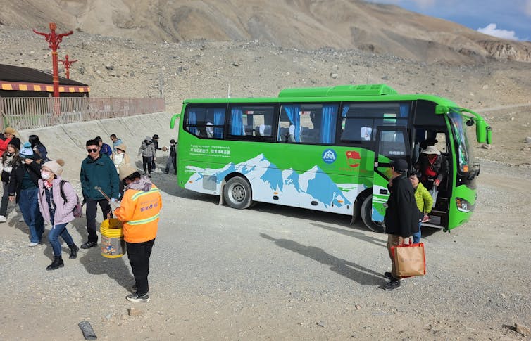 Tourists get out of a green electric bus.