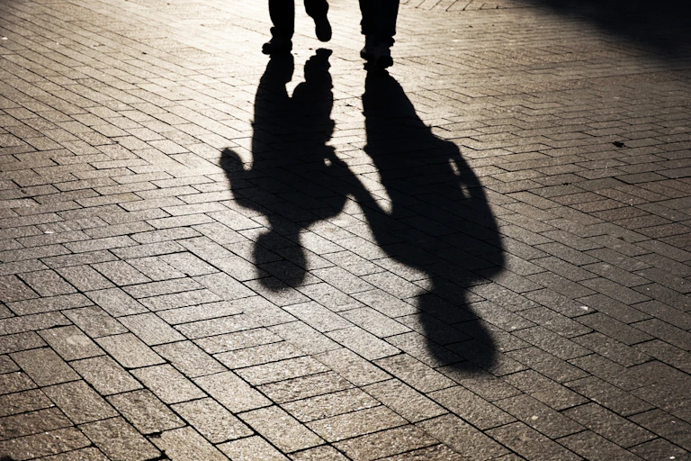 Silhouettes de deux personnes marchant dans la rue. Ombres d'adulte et d'enfant sur le trottoir.