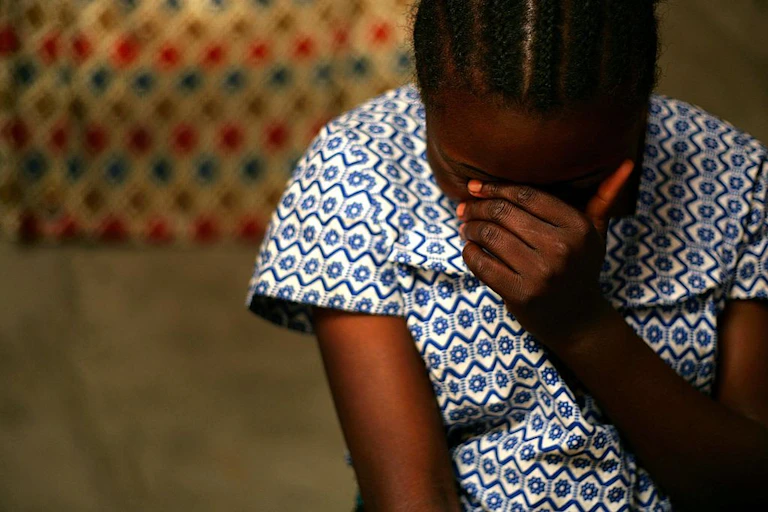 A woman with her head bowed, covering her face with a hand.