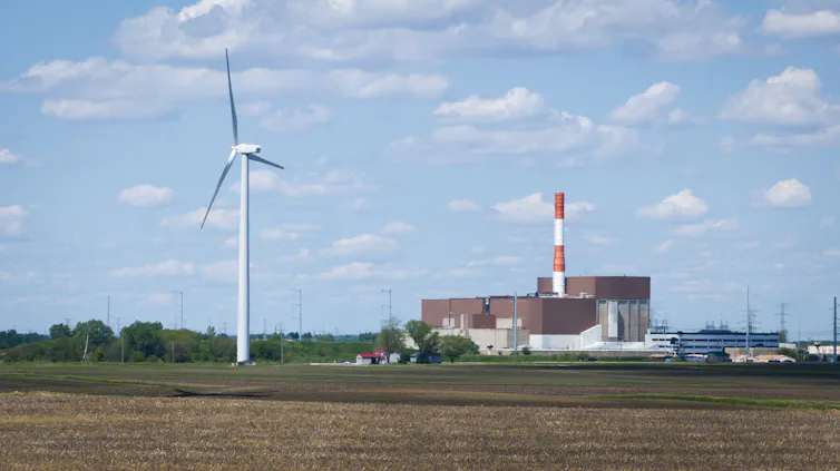 A wind turbine spins in an open space in front of a large collection of buildings.