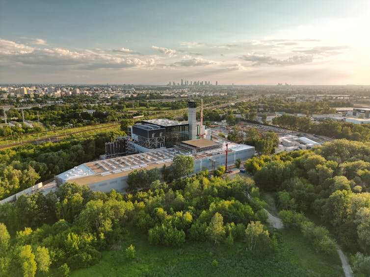 aerial view of waste incineration buildings surrounded by green countryside, city in distant backgroun