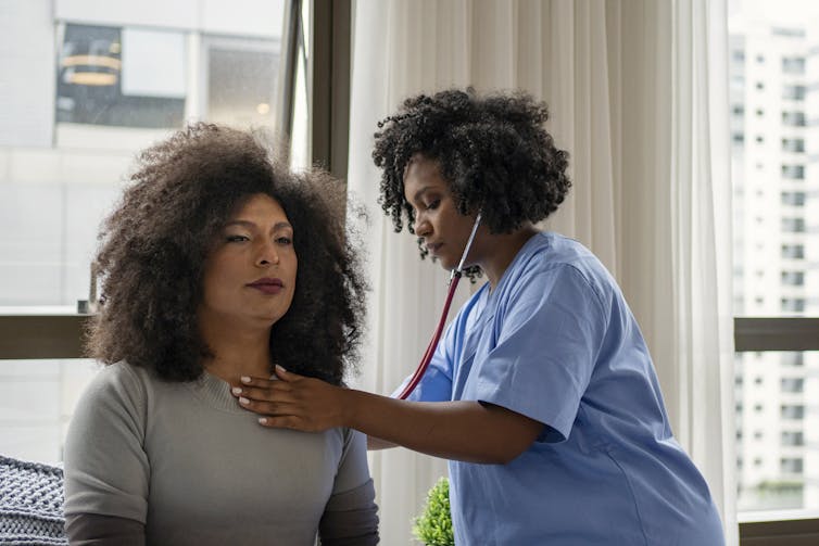Health care provider holding a stethoscope to a patient's back