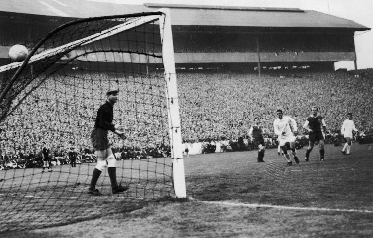A black-and-white photo shows a goal in the back of a soccer net and players on a field.