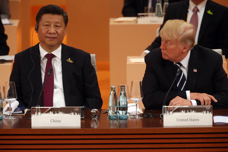 Two men in suits sit behind a desk.