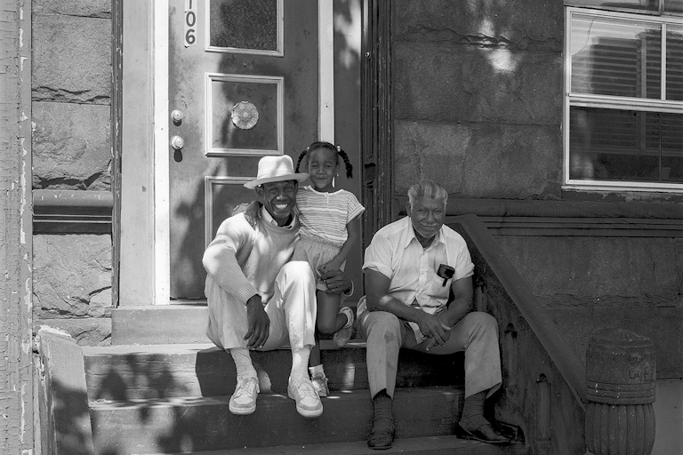 Portrait of young, smiling girl in pig tails with arm wrapped around smiling man, and an older gentleman sitting next to them