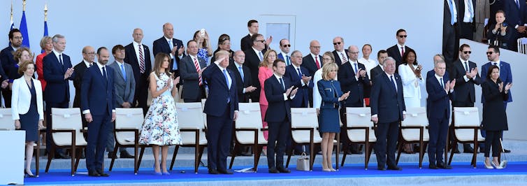 A line of dignitaries clapping and saluting as a parade goes by.