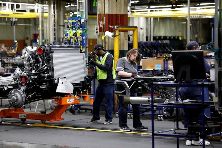 Workers are seen assembling car parts.