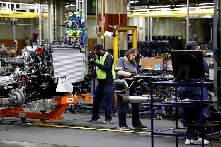 Workers are seen assembling car parts.