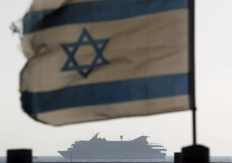 A ship on the horizon with a tattered Israeli flag in the foreground.