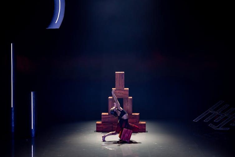 A woman dances in front of a tower of bricks.