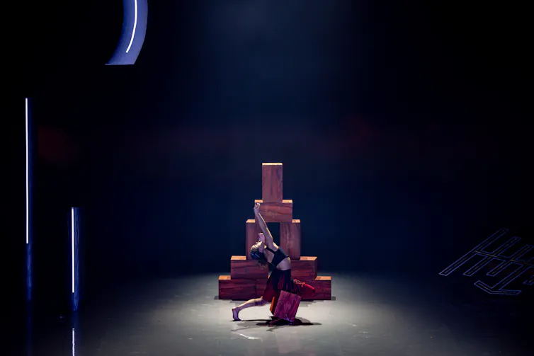 A woman dances in front of a tower of bricks.