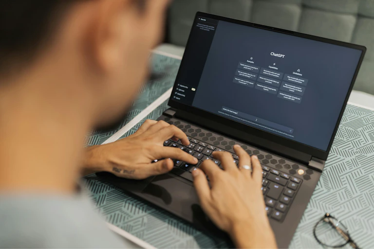 A man types on a laptop, ChatGPT is loaded on the screen.