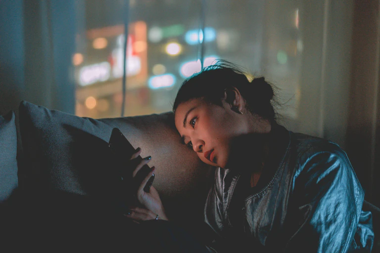 Woman sits in the dark, looking at her phone