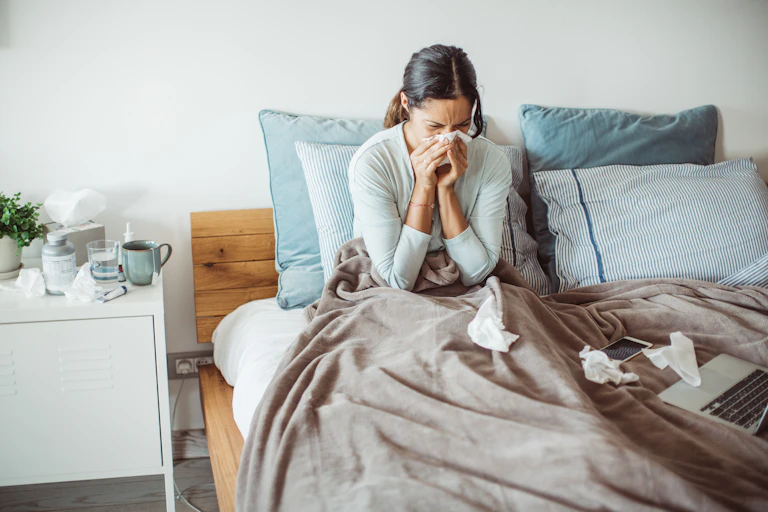 A woman sitting in bed blowing her nose.