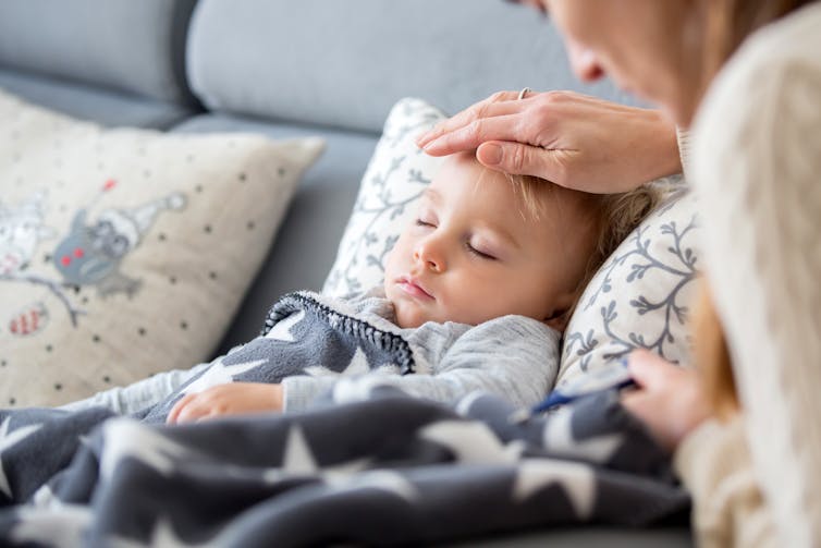 A mother holds her hand over a sleeping child's forehead.