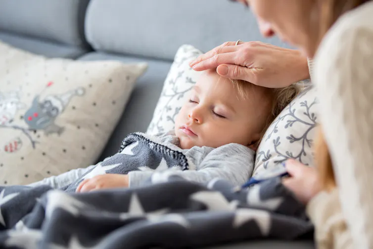A mother holds her hand over a sleeping child's forehead.