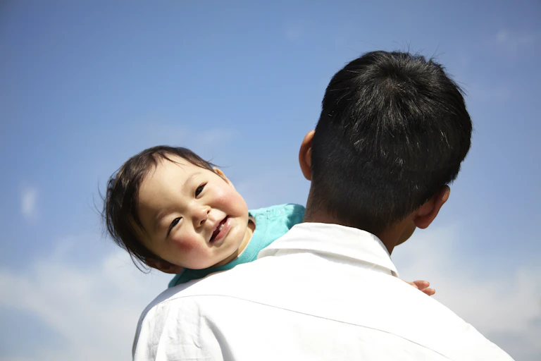 Toddler smiles over the shoulder of a man.