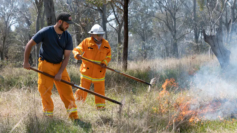 two people working with fire in grassy landscape.